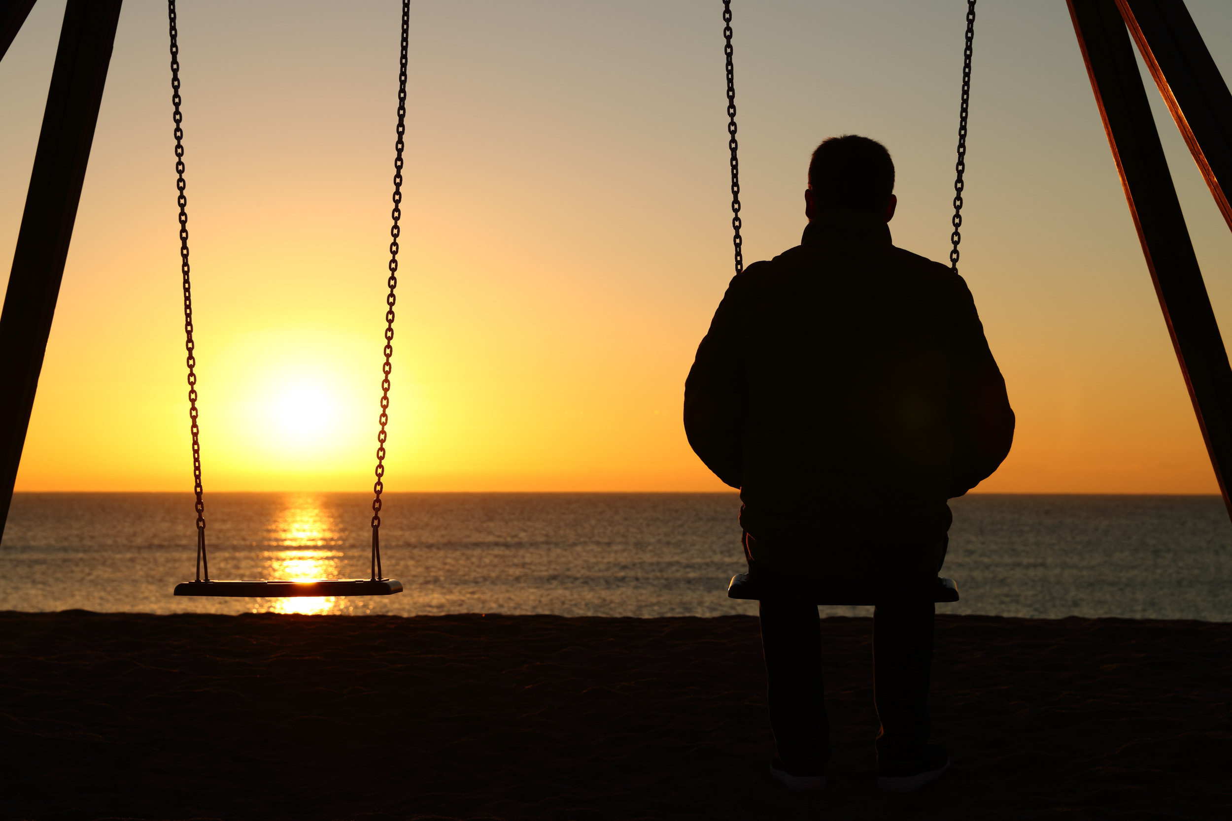 man on swing looking out to sunset