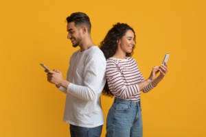 Young Couple Back-To-Back Yellow Background Mobile Phones