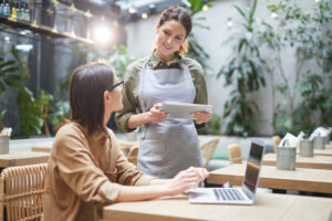 Woman with laptop speaking to waitress.