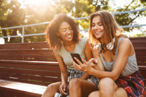 Two Women Smile Mobile Phone Park Bench