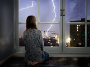 Woman looking out window during thunderstorm.