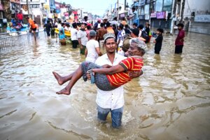 A youth carries an elderly man as they wade through a flooded street after heavy rainfall on the outskirts of Colombo on November 30, 2025. (Photo by Ishara S. KODIKARA / AFP)